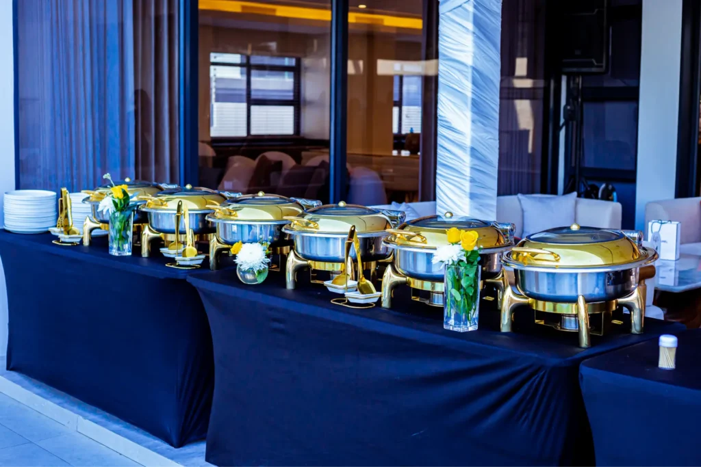 Food items kept in warmers on a blue themed buffet style table